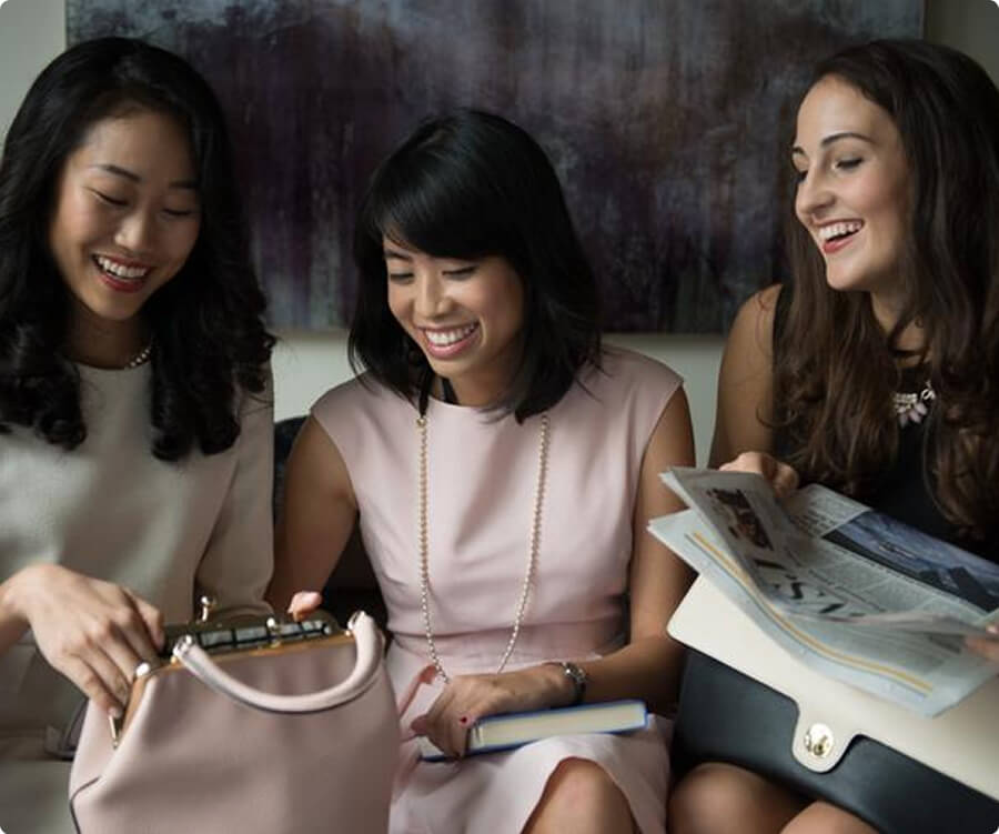 Three women smiling while looking into a handbag.